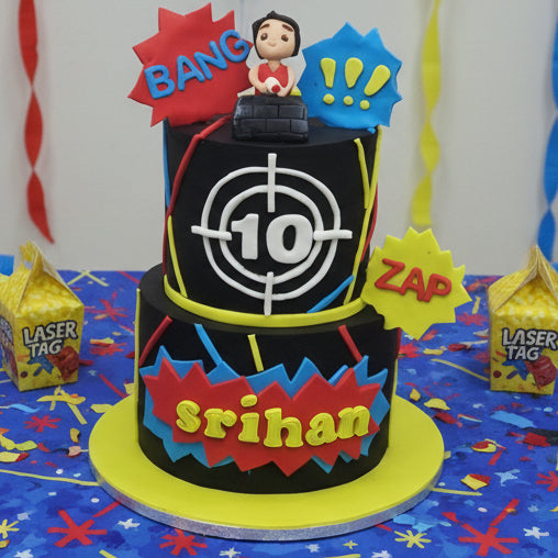A themed cake designed to look like a laser tag gun, with a figurine of a character holding a laser blaster, surrounded by bright neon lines and a black fondant wrap. Laser tag themed birthday cake made in Basildon Essex for kids celebration