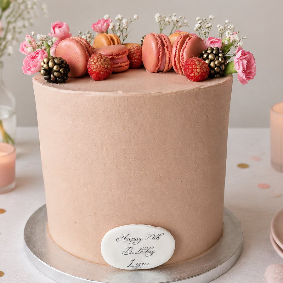 Elegant buttercream celebration cake decorated with flowers, macarons and berries, available for delivery across Essex from CakeObsession.