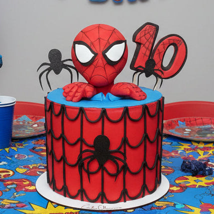 Spider-Man themed birthday cake with spider decorations on a colorful tablecloth.