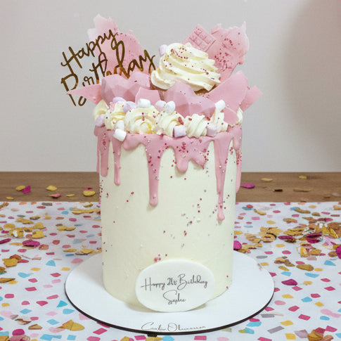 Pink birthday cake with white frosting, sprinkles, and 'Happy Birthday' topper on a white background.