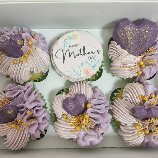 Decorative cupcakes with purple and white frosting, gold accents, and a 'Happy Mother's Day' sign.