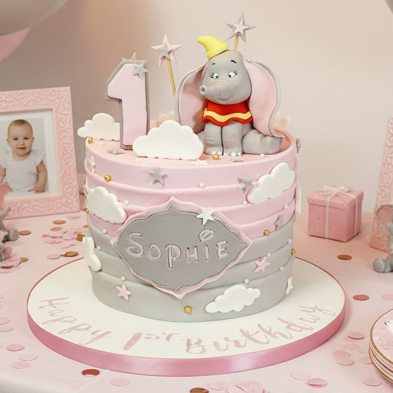Dumbo-themed birthday cake in Basildon Essex, Victoria sponge or chocolate cake with pink and grey fondant, Dumbo figurine and fluffy clouds.