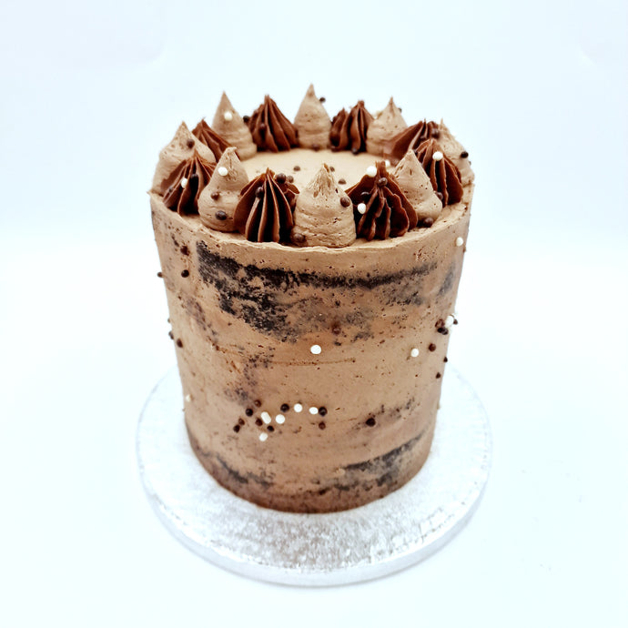 A semi-naked cake features layers of fluffy sponge, adorned with a light buttercream coating, revealing hints of the cake beneath.