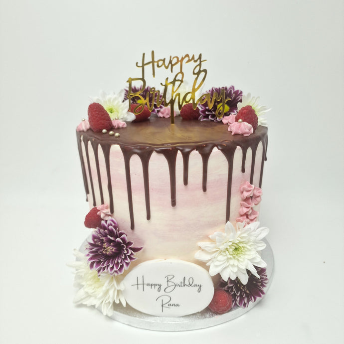  A beautifully decorated white buttercream cake with a pink chocolate drip, topped with fresh berries and delicate flowers, perfect for elegant celebrations.