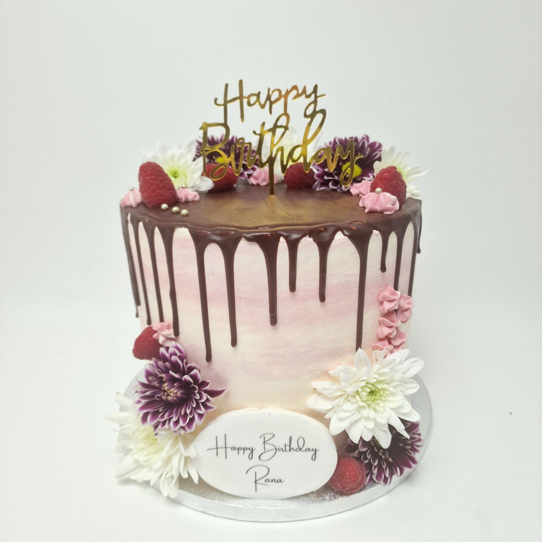  A beautifully decorated white buttercream cake with a pink chocolate drip, topped with fresh berries and delicate flowers, perfect for elegant celebrations.