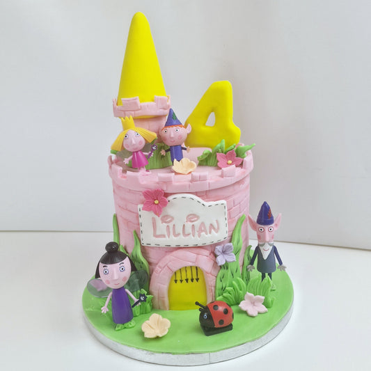 A decorative cake designed to look like a pink castle with characters around it, including a yellow gnome-like figure on top, and a green caterpillar-like creature on the grass.