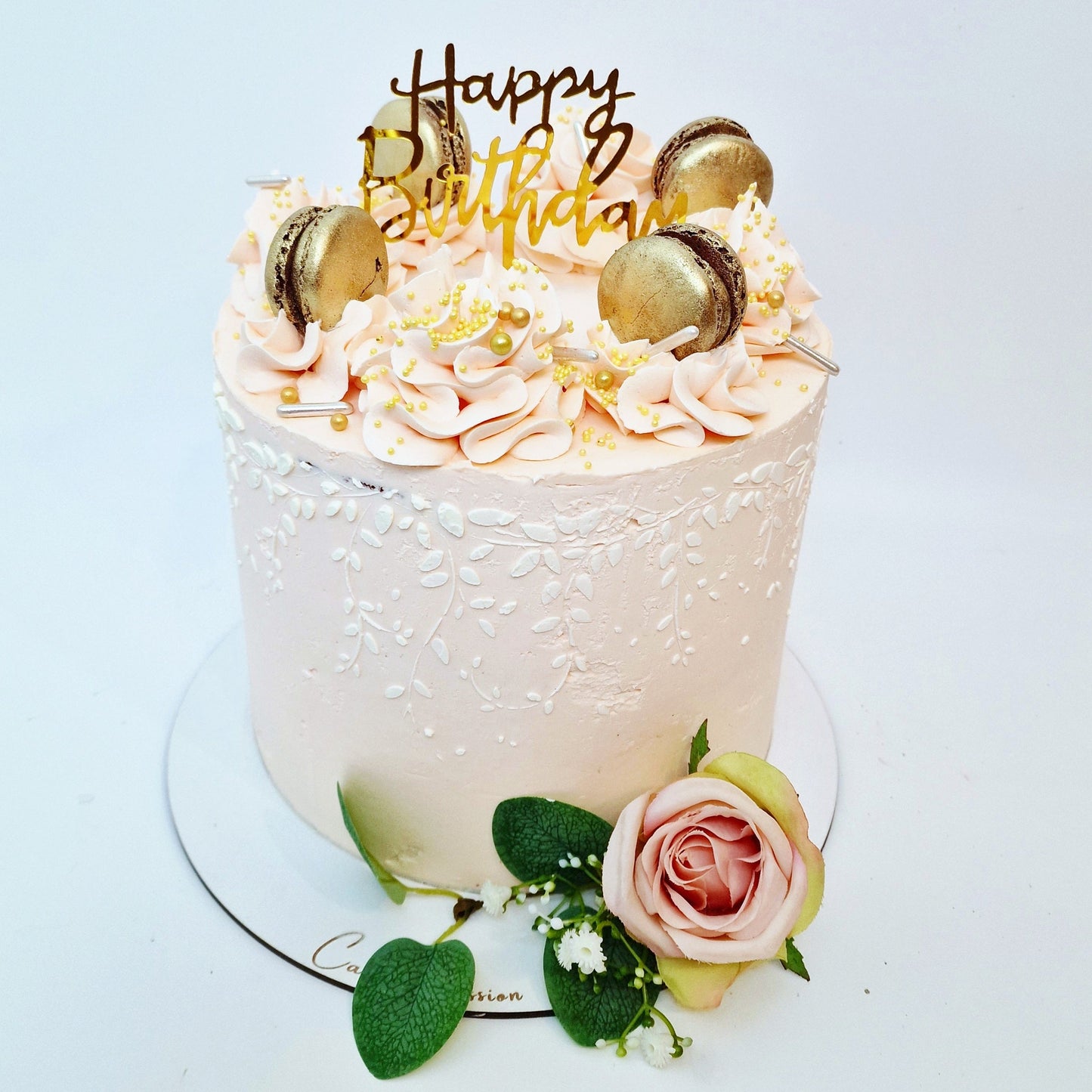 Birthday cake with pink frosting, gold accents, and a 'Happy Birthday' topper on a white background.