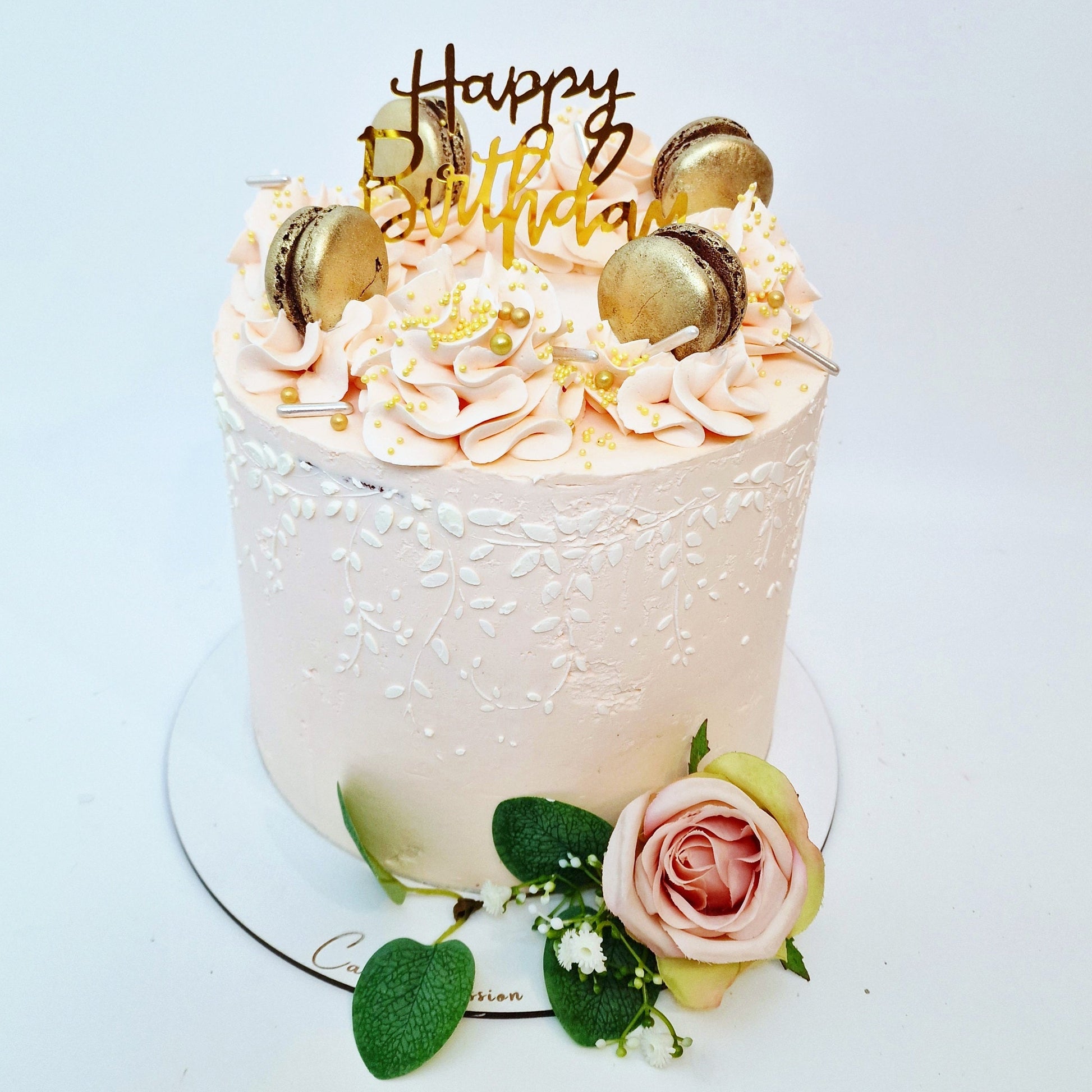 Birthday cake with pink frosting, gold accents, and a 'Happy Birthday' topper on a white background.