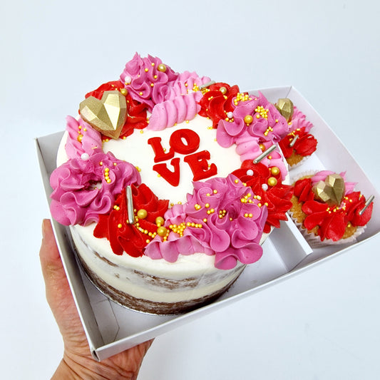 Small Valentine’s cake for two. A gift set with 2 matching cupcakes. White frosting with pink swirls on top.