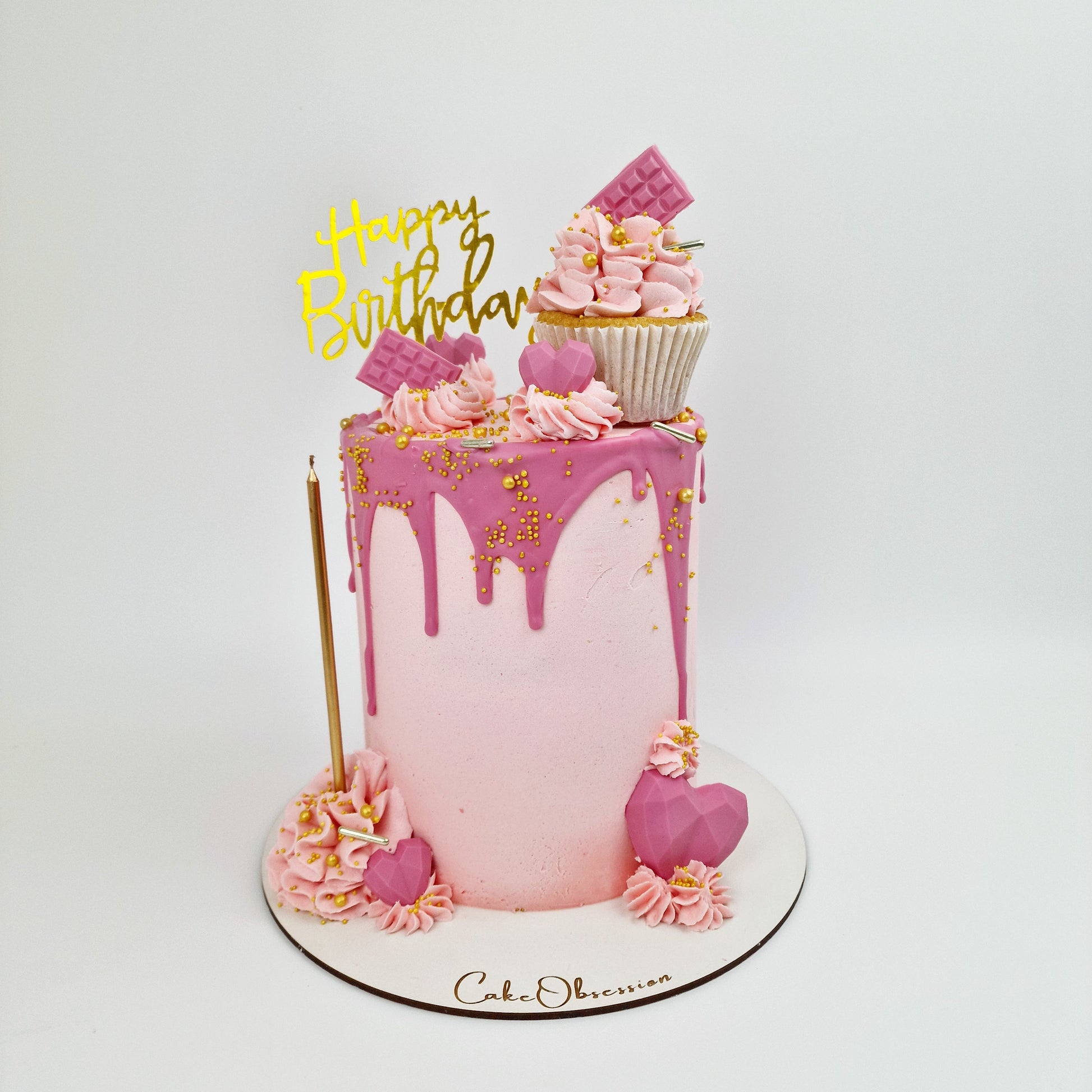 Pretty in Pink Celebration Cake with smooth baby pink buttercream, hot pink drip, cupcake topper, mini hearts, chocolates, and golden candle, handmade and personalised, perfect for birthdays, anniversaries, and special celebrations, available for delivery in Basildon and Essex.
