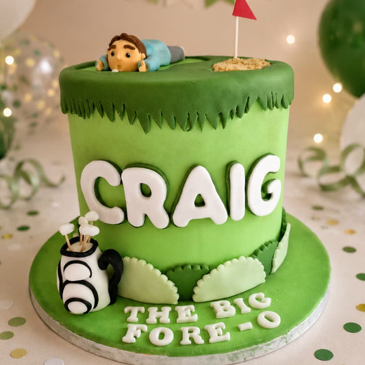A custom green fondant cake designed like a golf course, with the name 'CRAIG' in large white letters on the side, a small golf ball and club decoration, a mini flag, and 'THE BIG FORE-O' written on the base. A small figurine is visible at the top edge.