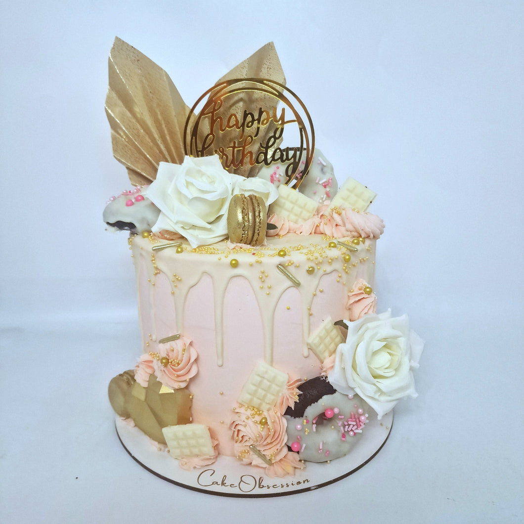 This exquisite pink cake is adorned with two golden fans and silk roses, creating a stunning visual display. It features a luscious white chocolate drip, golden macaroons, and a heart-shaped accent for added elegance. A perfect choice for a romantic or celebratory occasion.
