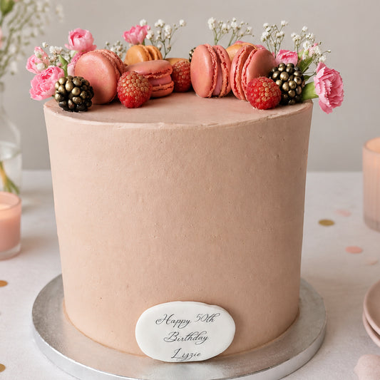 Elegant buttercream celebration cake decorated with flowers, macarons and berries, available for delivery across Essex from CakeObsession.