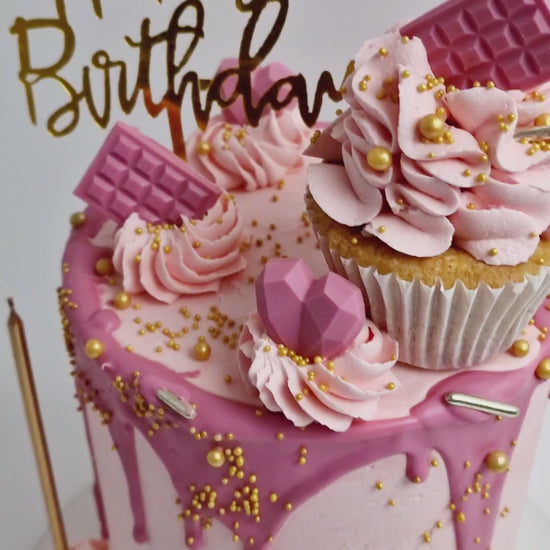 Pretty in Pink Celebration Cake with smooth baby pink buttercream, hot pink drip, cupcake topper, mini hearts, chocolates, and golden candle, handmade and personalised, perfect for birthdays, anniversaries, and special celebrations, available for delivery in Basildon and Essex.