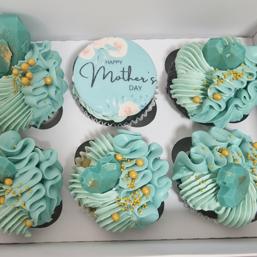 Box of cupcakes with Tiffany blue frosting and gold accents, featuring a 'Happy Mother's Day' cupcake.