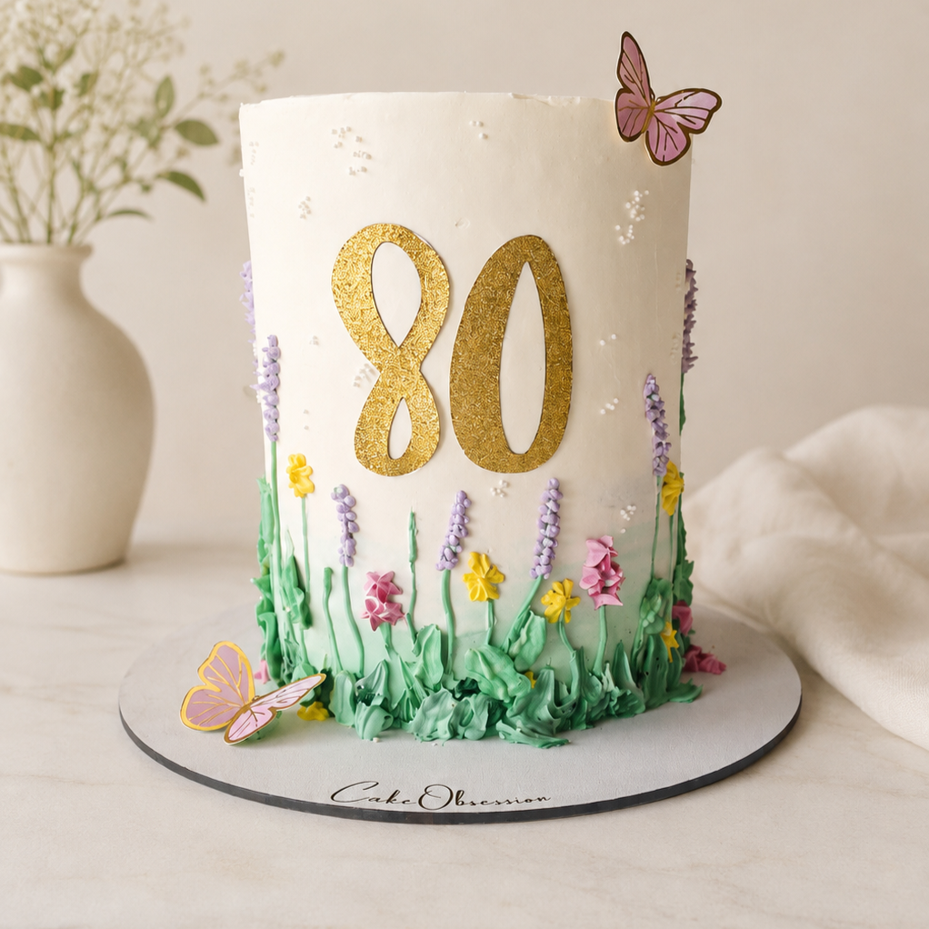 Wildflower birthday cake with white buttercream, colourful piped flowers, green grass, butterflies and personalised gold 80 topper, CakeObsession Basildon Essex.